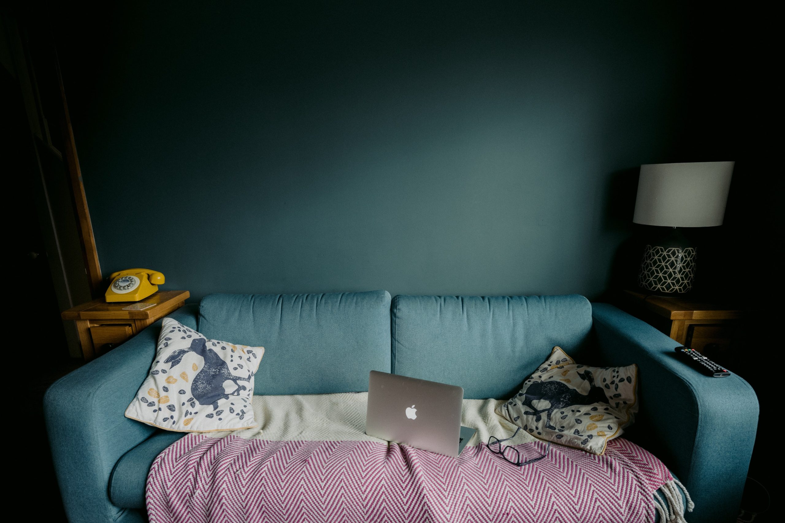 divano verde su parete azzurra con computer e coperta - lavorare da casa senza imbruttirsi