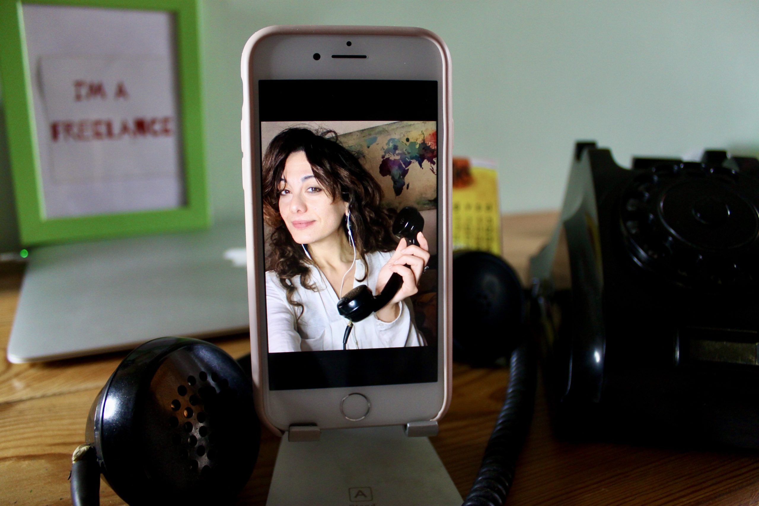 sabrina ripresa nello schermo di un iPhone, con una cornetta di antico telefono analogico in mano_Sfondo di una scrivania_video chiamate di lavoro_errori